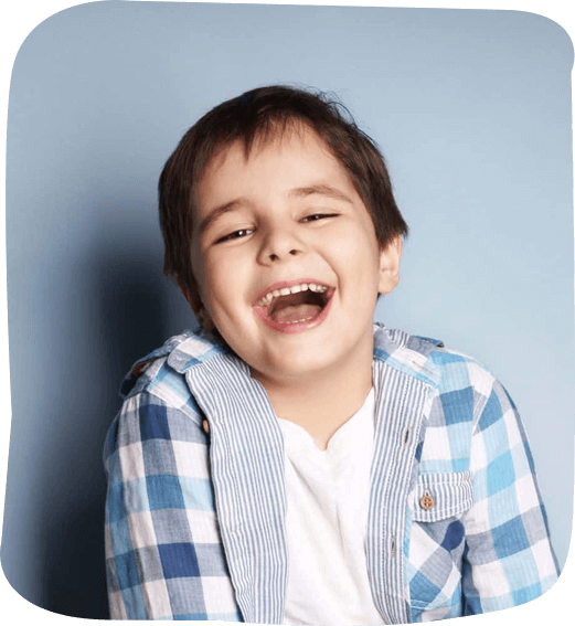 Young boy smiling brightly at camera, wearing blue plaid shirt against blue background.
