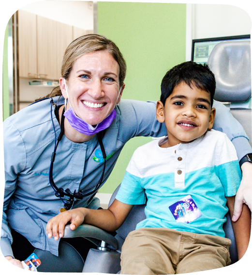 Pediatric dentist with stethoscope posing with young boy patient in dental office setting.