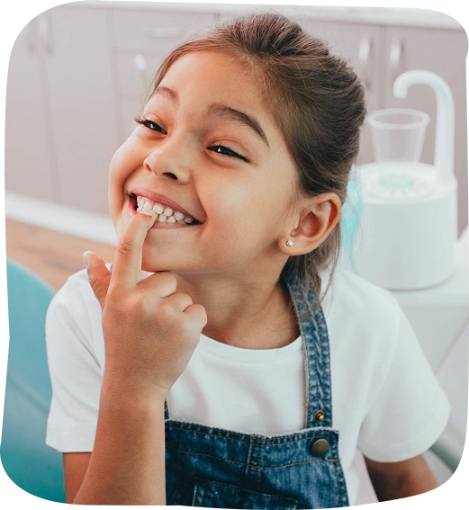 Smiling child pointing to teeth in bathroom, promoting pediatric dental health and hygiene.