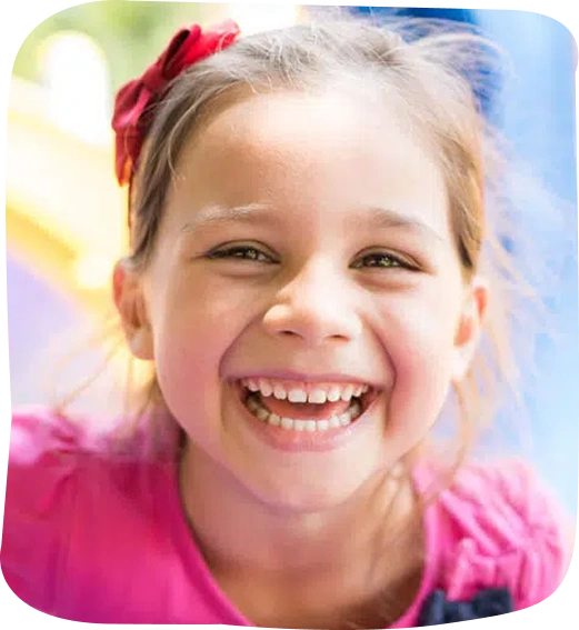 Young girl smiling brightly outdoors, showing healthy teeth and happy expression.